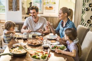 Happy parents and their small kids communicating while having lunch together at dining table at home.