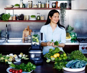 Tess Masters in a kitchen with green vegetables covering table