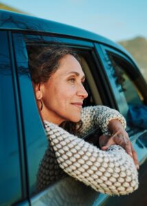 Smiling mature woman looking out at the view through a car window during a summer road trip in scenic countryside with a group of female friends