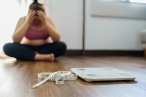 Woman sitting upset bored of dieting for weight loss, in front of a scale and tape measure