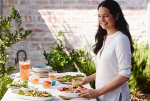 Tess Standing in front of a table making a yummy salad holding the dressing and a fruit juice on the table