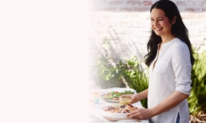 Tess Standing in front of a table making a yummy salad holding the dressing