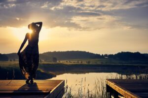 Silhouette of a women doing a yoga pose in front of a beautiful sunset and lake