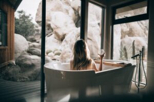 Back of a women in a bath with a beautiful house setting drinking from a glass