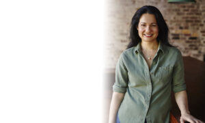Tess Masters smiling in a green button down shirt in front of brick wall